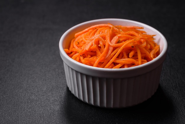 Gustosa carota coreana piccante con spezie ed erbe aromatiche su uno sfondo di cemento scuro