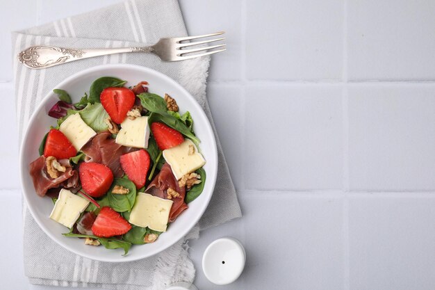 Gustosa insalata con formaggio brie, prosciutto, fragole e noci servite su un tavolo piastrellato bianco a disposizione piatta Spazio per il testo