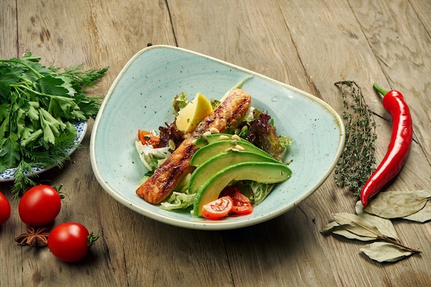 Gustosa insalata con salmone grigliato, avocado, lattuga in una ciotola blu su un tavolo di legno. Insalata di mare