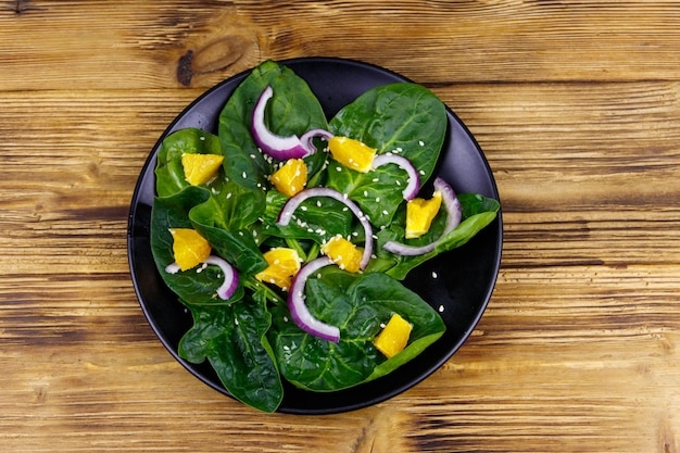 Gustosa insalata con spinaci arancio cipolla rossa e semi di sesamo su tavola di legno Vista dall'alto Cibo sano o concetto vegetariano