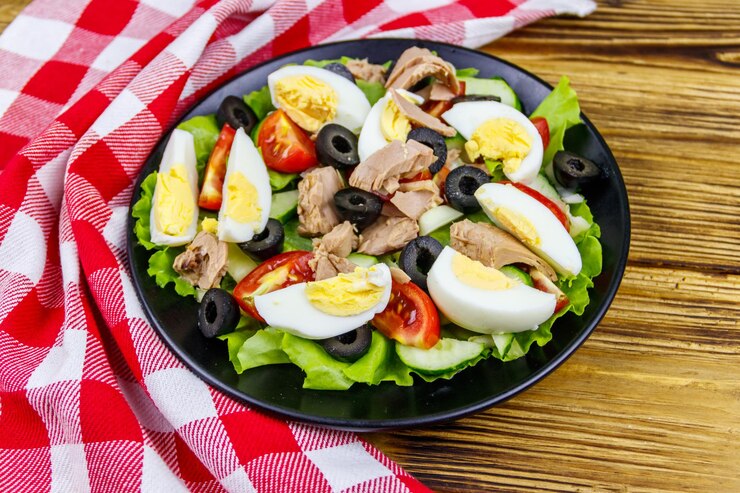 Gustosa insalata di tonno con lattuga olive nere uova e verdure fresche sulla tavola di legno