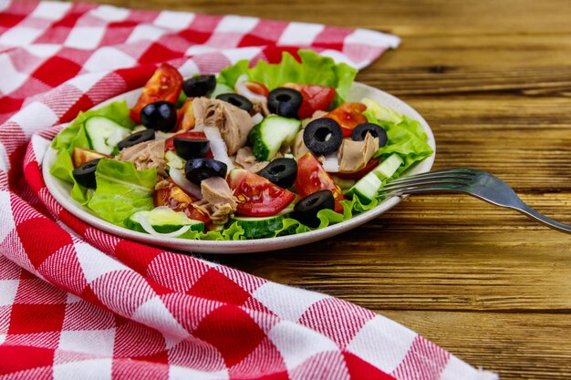 Gustosa insalata di tonno con olive nere di lattuga e verdure fresche sulla tavola di legno