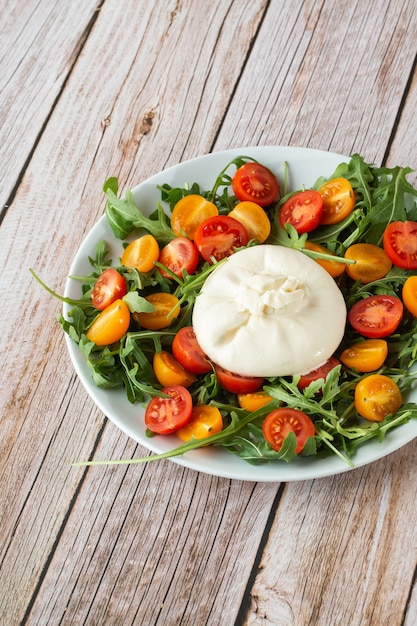 Gustosa insalata fresca con mozzarella burrata, rucola, pomodorini e basilico su un piatto bianco