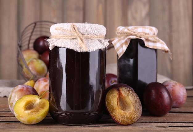 Gustosa marmellata di prugne in barattoli e prugne su tavola di legno su sfondo di legno