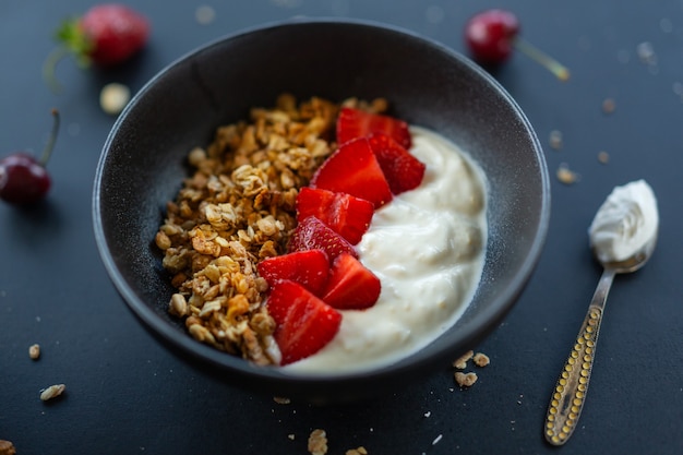 Gustosa muesli fruttata fatta in casa servita in una ciotola con yogurt su sfondo scuro. Avvicinamento