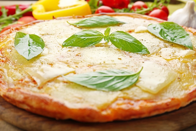 Gustosa pizza decorata con basilico e verdure su fondo di legno da vicino