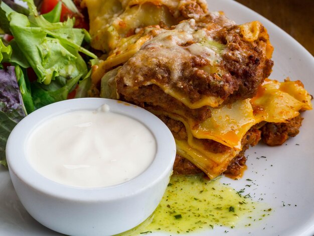 Gustosa porzione di lasagne tradizionali italiane con carne macinata piccante a base di pomodoro e mozzarella fusa tra strati di pasta con panna e foglie verdi