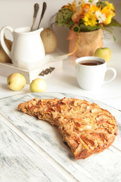 Gustosa torta di mele appena sfornata con mele e tazza da tè sullo sfondo. Concetto di cibo sano fatto in casa.