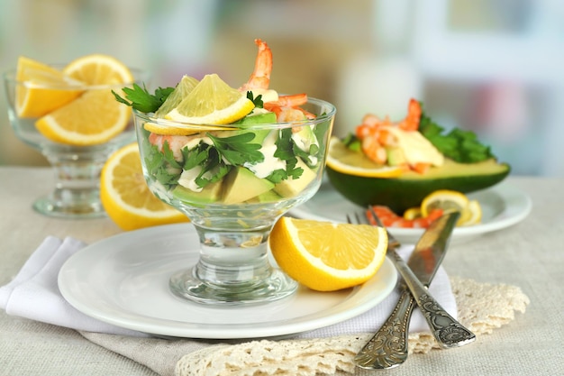 Gustose insalate con gamberi e avocado in una ciotola di vetro e su un piatto sul tavolo su sfondo luminoso