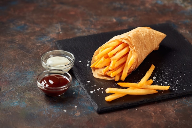 Gustose patatine fritte con salse sul tagliere di ardesia, su sfondo scuro