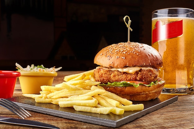 Gustose patatine fritte di hamburger con salsa e bicchiere di birra su tavola nera