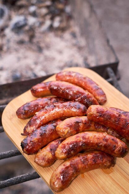 Gustose salsicce appena grigliate sulla griglia a carbone sul tagliere di legno