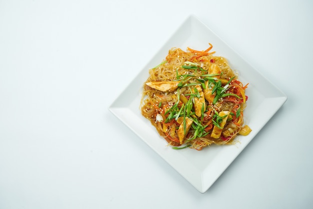 Gustose tagliatelle di udon in salsa agrodolce con verdure e piatto di carne di pollo su un tavolo grigio. Vista dall'alto con spazio di copia