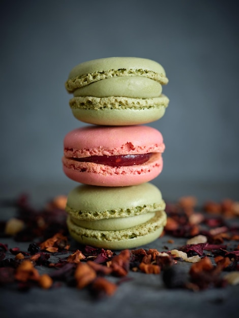 Gustosi amaretti al pistacchio e alla fragola posti uno sopra l'altro vicino alle foglie di tè della frutta secca su sfondo grigio sfocato