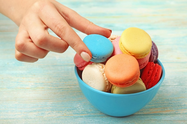 Gustosi amaretti colorati in ciotola e mano femminile su sfondo di legno colorato