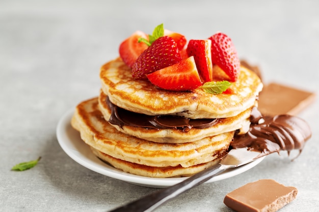 Gustosi appetitosi pancake appena sfornati decorati con pasta di fragole e cioccolato serviti a colazione. Avvicinamento