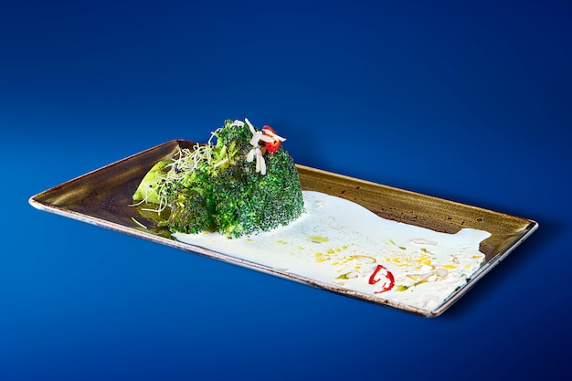 Gustosi broccoli con salsa allo yogurt, peperoncino e spezie su un elegante piatto nero. Ristorante che serve cibo. Cibo vegetariano. Avvicinamento..