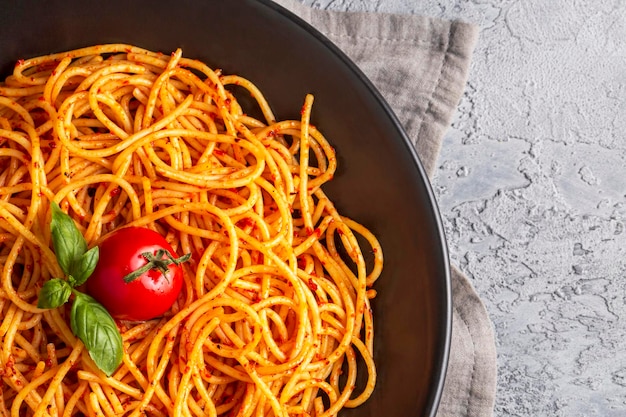 Gustosi e appetitosi spaghetti italiani classici con salsa di pomodoro, parmigiano e basilico sul piatto e ingredienti per cucinare la pasta sul tavolo di marmo bianco.
