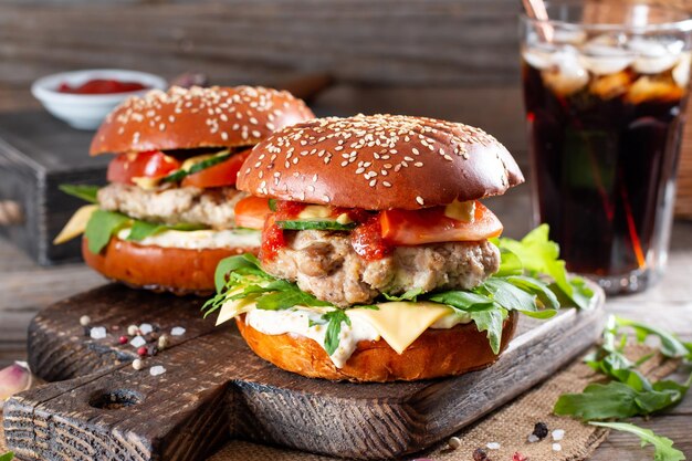 Gustosi hamburger fatti in casa alla griglia con carne di manzo, pomodoro, formaggio e rucola su fondo di legno rustico. Concetto di fast food e cibo spazzatura.