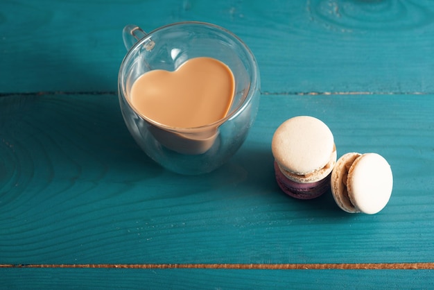 Gustosi macarons alle mandorle e caffè con latte sulla superficie del legno blu Stile romantico vintage