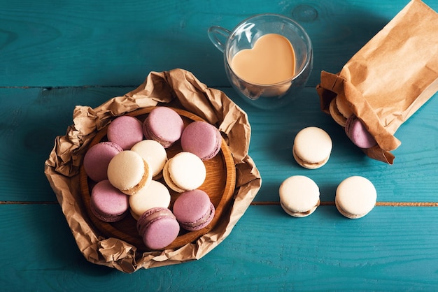 Gustosi macarons alle mandorle e caffè con latte sulla superficie del legno blu Stile romantico vintage