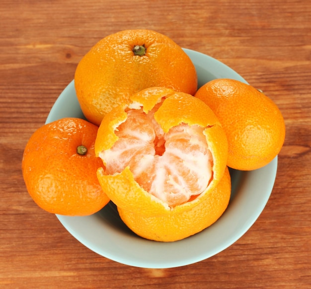 Gustosi mandarini in ciotola di colore su sfondo di legno