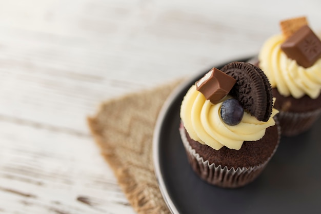 Gustosi muffin multicolori e cupcakes su un vassoio, tavolo in legno. Decorato con diverse caramelle, biscotti, mirtilli e crema di formaggio dolce colorata sulla parte superiore.