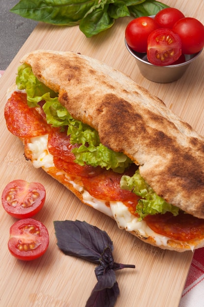 Gustosi panini ai peperoni con crema di formaggio e insalata su una tavola di legno