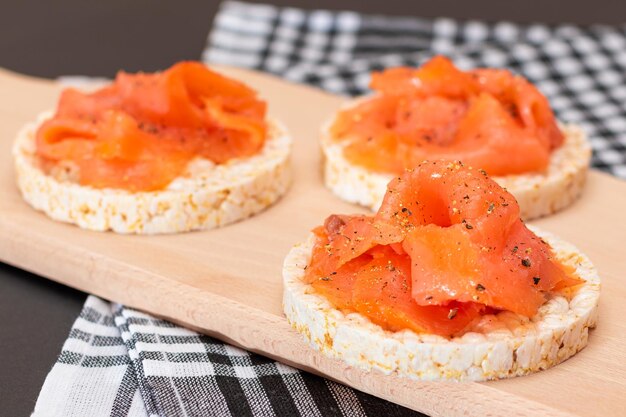 Gustosi panini alla torta di riso con fette di salmone fresco su tagliere di legno Colazione facile e cibo dietetico Pane croccante con pesce rosso Spuntino dietetico sano