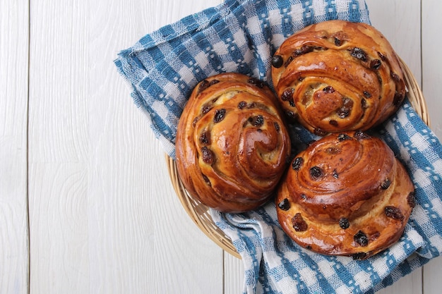 Gustosi panini con uvetta in un cesto su uno sfondo di legno bianco posto per la colazione da forno fresco per la vista dall'alto del testo