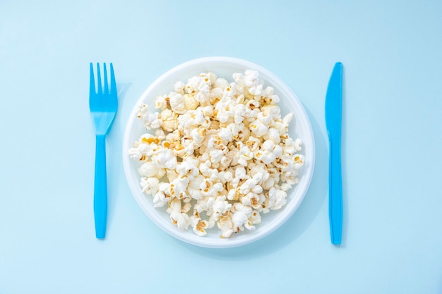Gustosi popcorn salati in ciotola di plastica e posate su blu Cinema e concetto di intrattenimento