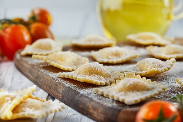 Gustosi ravioli crudi con farina, pomodorini, olio di semi di girasole e basilico su una superficie in legno chiaro