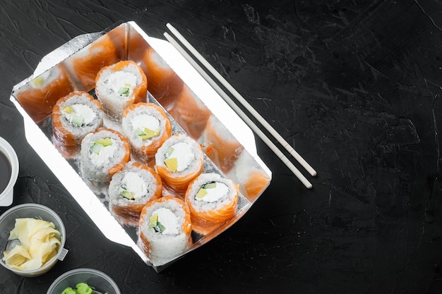 Gustosi rotoli di sushi in scatole usa e getta, su sfondo di pietra nera, con copyspace e spazio per il testo