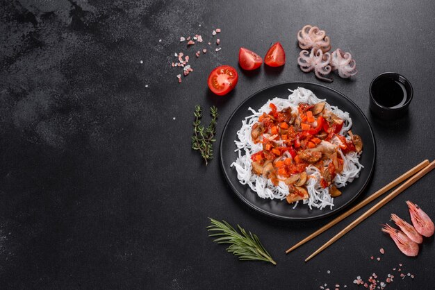 Gustosi spaghetti di riso con pomodoro, peperone rosso, funghi e frutti di mare su uno sfondo di cemento scuro