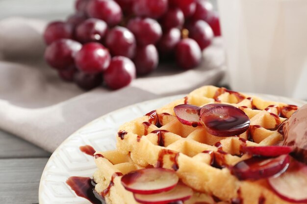 Gustosi waffle con delizioso gelato all'uva e sciroppo su piatto bianco da vicino