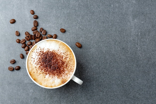 Gustoso cappuccino appetitoso in tazza con fagioli sul tavolo di cemento.