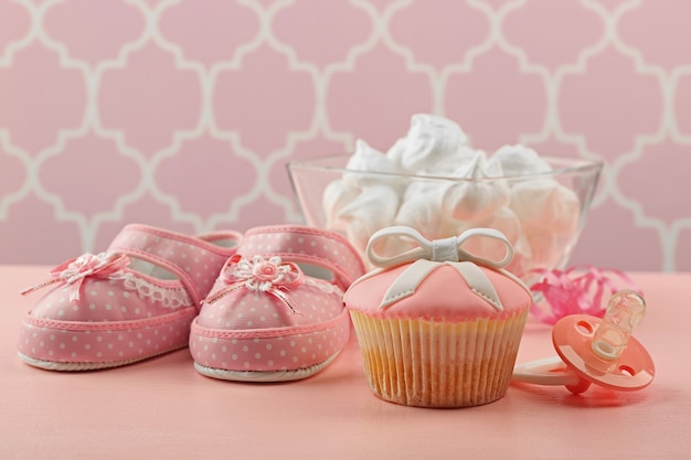 Gustoso cupcake con fiocco e scarpe per bambini, ciuccio su sfondo colorato