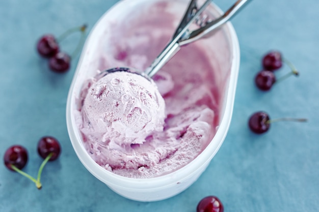 Gustoso gelato rinfrescante con ciliegia in scatola di plastica su sfondo luminoso. Avvicinamento.