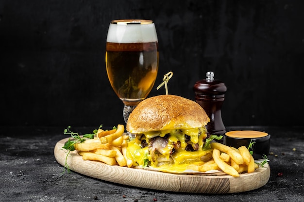 Gustoso hamburger grande e bicchiere di birra su vassoio di legno Concetto di cibo americano fast food banner menu ricetta posto per il testo