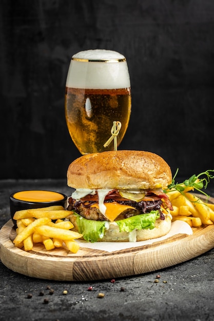 Gustoso hamburger grande e bicchiere di birra su vassoio di legno Concetto di cibo americano fast food banner menu ricetta posto per il testo