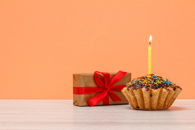 Gustoso muffin di compleanno con glassa al cioccolato e caramello, decorato con una candela festosa accesa e una confezione regalo sullo sfondo della pesca. Buon compleanno concetto minimo.