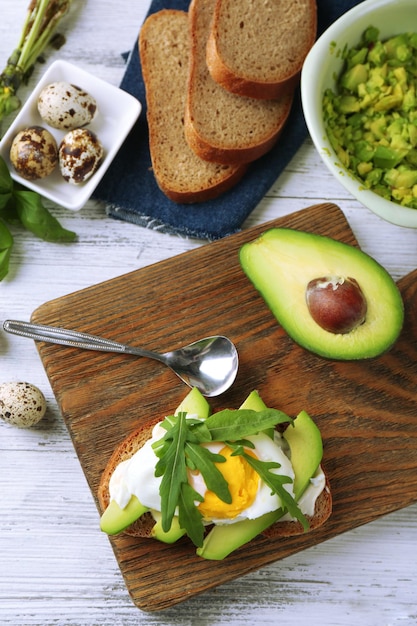 Gustoso panino con uovo avocado e rucola su fondo di legno