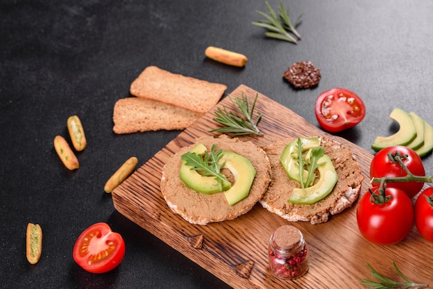 Gustoso panino fresco con pasta di fegato, pezzi di avocado e una rucola su un tavolo di cemento scuro