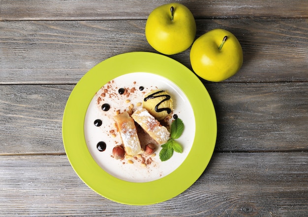 Gustoso strudel di mele fatto in casa con noci, foglie di menta e gelato su piatto, su fondo di legno