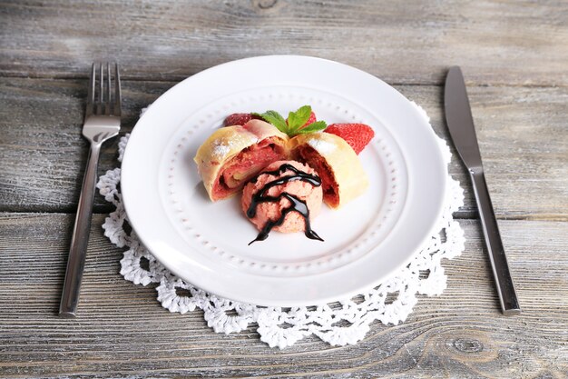 Gustoso strudel fatto in casa con gelato, fragole fresche e foglie di menta su piatto, su fondo di legno