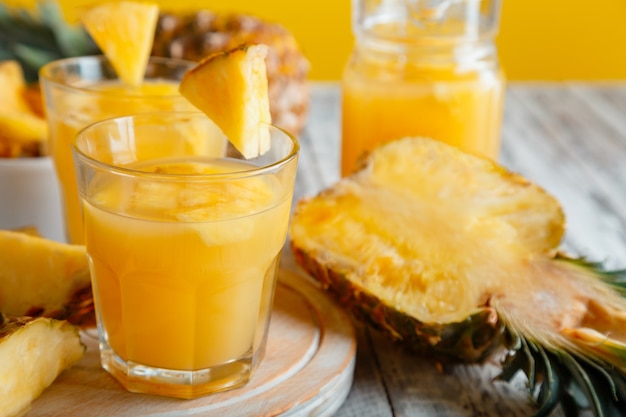 Gustoso succo di ananas in vetro con fette di frutta di ananas. Cocktail e succo di ananas naturali freschi in vetro sulla tavola di legno bianca. Foto d'archivio di alta qualità.