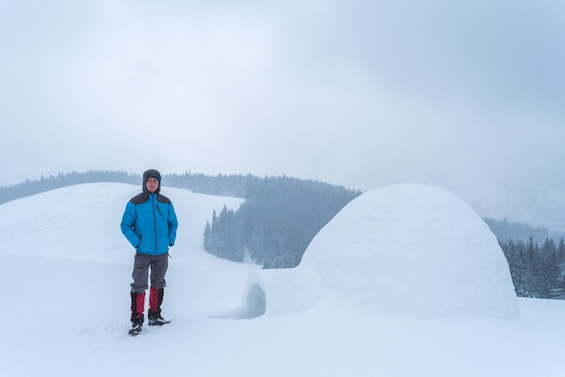 Guy ha costruito un igloo in montagna. Avventure invernali nell'escursione. Paesaggio con una giornata nuvolosa nebbiosa