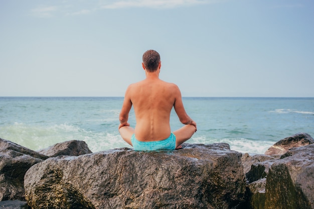 Guy meditando al tramonto seduto su una roccia in riva al mare