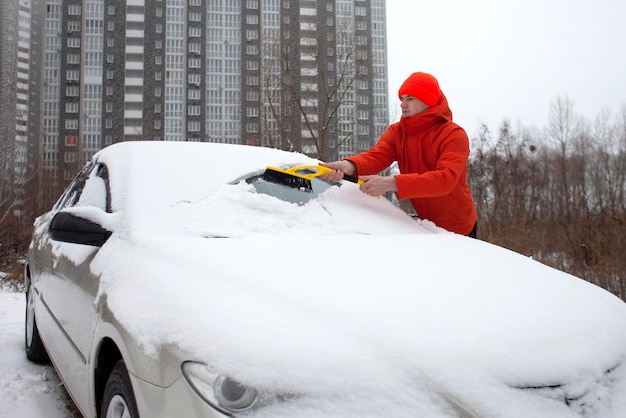 Guy pulisce la neve con un pennello dall'auto un uomo si prende cura dell'auto in inverno
