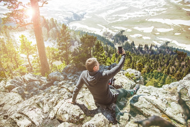 Guy Traveller scatta foto di sé su uno smartphone sullo sfondo delle montagne.